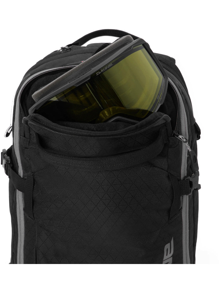 Close-up of the Dakine Heli 2.0 Pro Pack 20L in Black showing a ski goggle stowed in the open top pocket