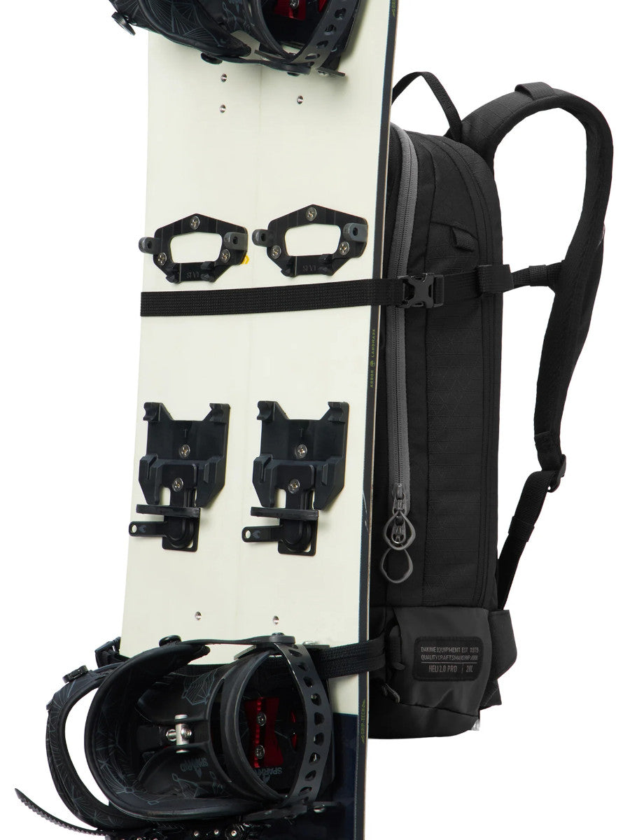Dakine Heli 2.0 Pro Pack 20L in Black carrying a splitboard vertically on the front panel, side view showing the shoulder strap