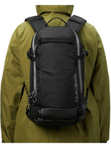 Person in an olive jacket wearing the Dakine Heli 2.0 Pro Pack 20L in Black, rear view showing the shoulder straps and fit