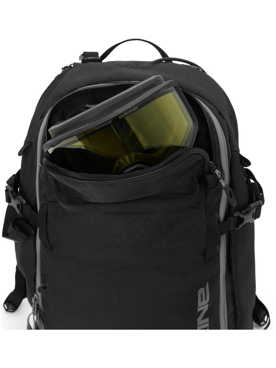 Close-up of the Dakine Heli 2.0 Pro Pack 26L in Black showing a ski goggle stowed in the unzipped top pocket