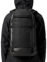 Person in a black hooded jacket wearing the Dakine Heli 2.0 Pro Pack 26L in Black, rear view showing how it sits on the back
